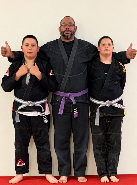 Coach Jay standing with two young jiu-jitsu students in black gis